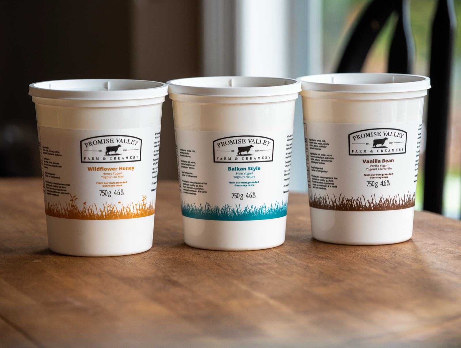 Three Promise Valley Farm yogurt containers lined up, showing Wildflower Honey, Balkan Style, and Vanilla Bean flavours with colour-coded grass illustrations